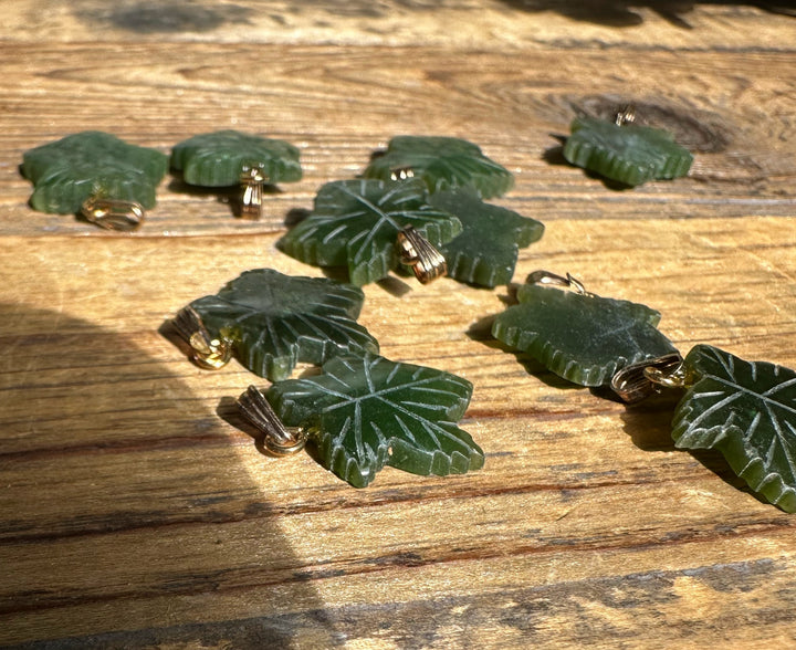 Green maple leaf pendants with gold-tone bails scattered on a wooden surface