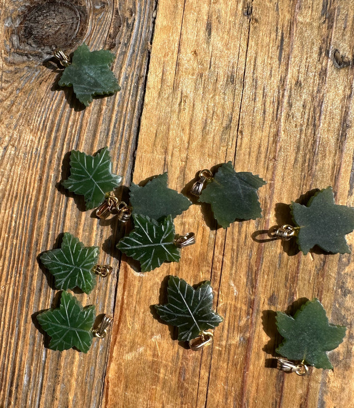 Assorted green maple leaf pendants with gold bails arranged on a wood background