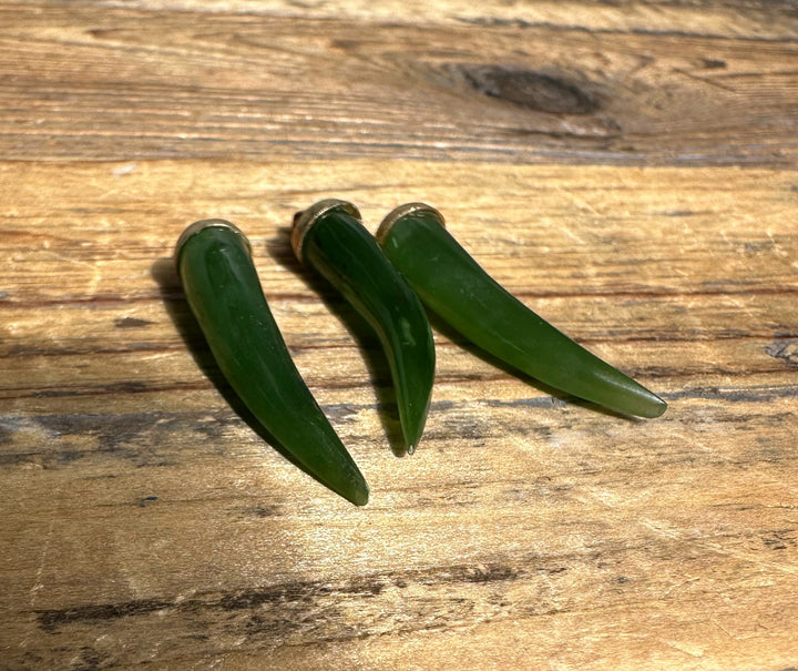 Three green jade horn pendants with metal caps on a wooden surface.