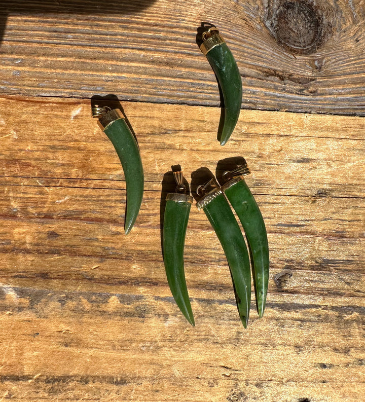 Group of four green jade horn pendants with brass caps arranged on a wooden surface.