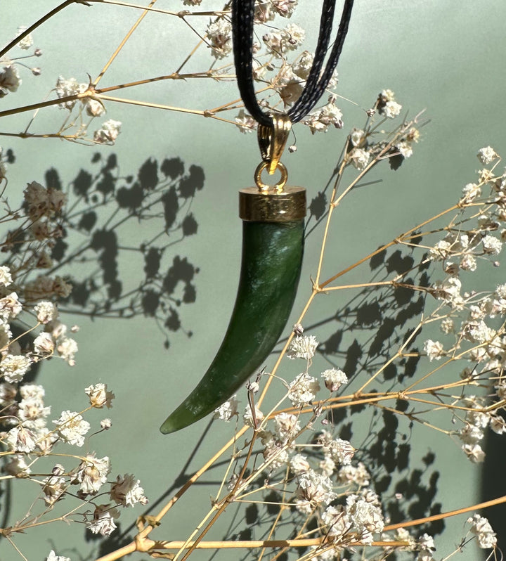 Green jade horn pendant on black cord with brass cap, photographed among dried white flowers.