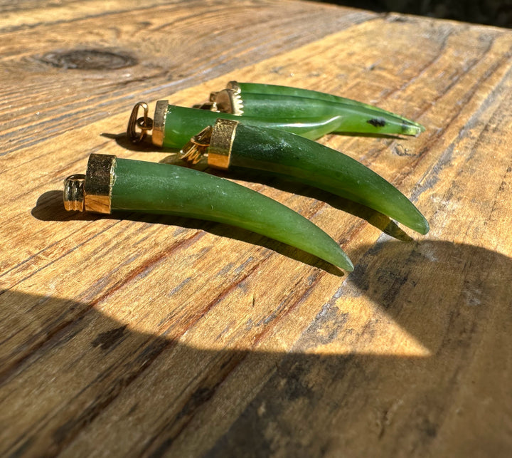 Three jade horn pendants with brass caps on a sunlit wooden surface