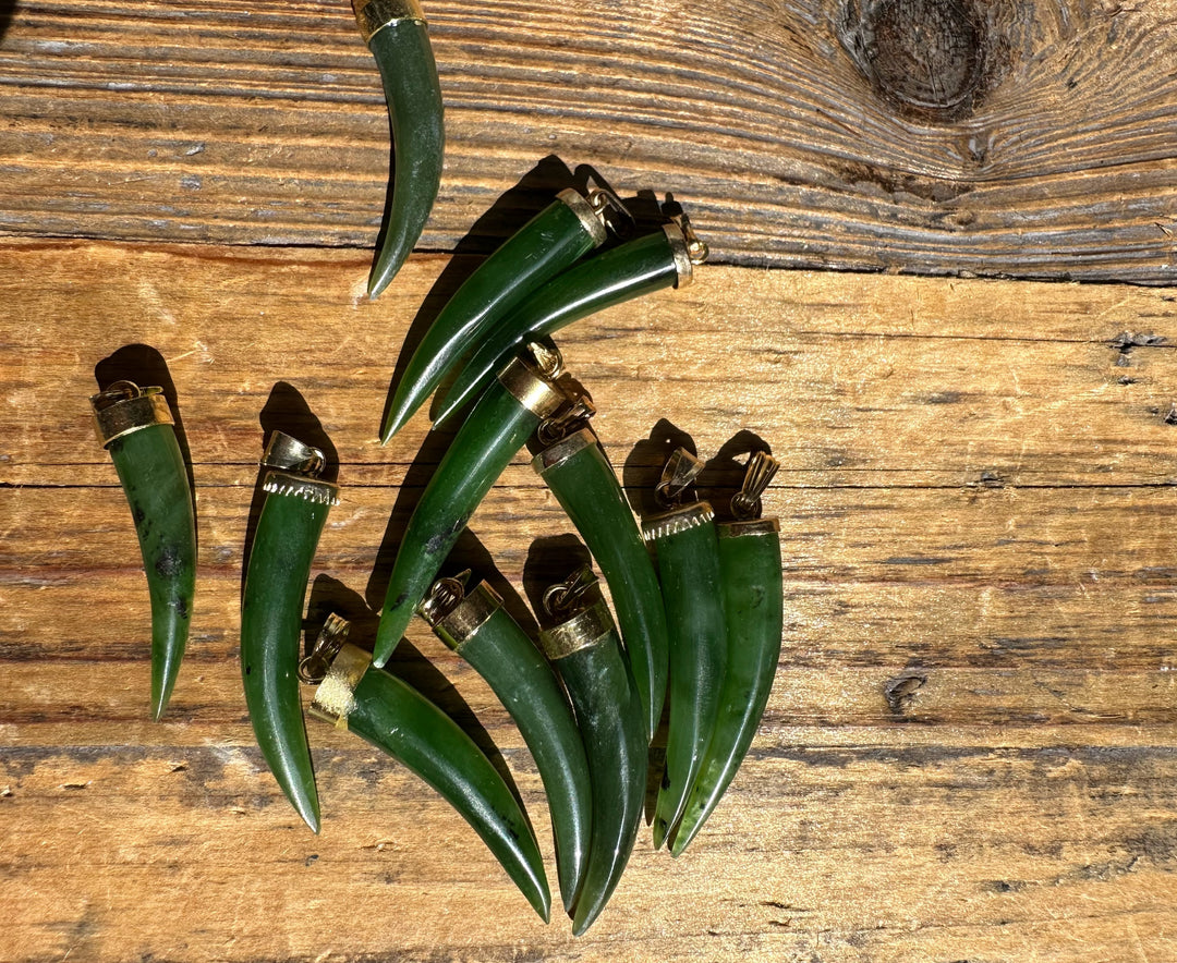 Green jade horn pendants with brass caps arranged on a rustic wooden surface