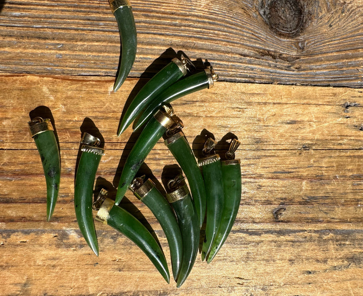 Green jade horn pendants with brass caps arranged on a rustic wooden surface