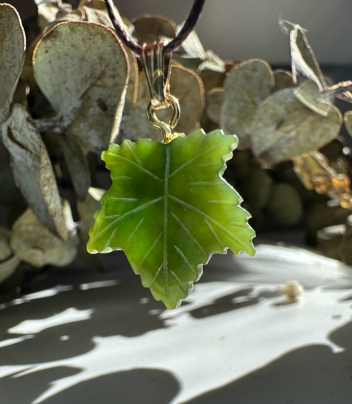 Bright green maple leaf pendant hanging from a brown cord with visible vein details.