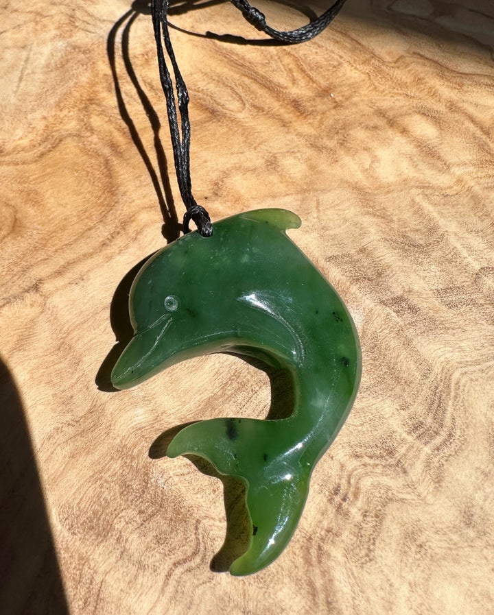 Green dolphin pendant on a black cord resting on a wood surface