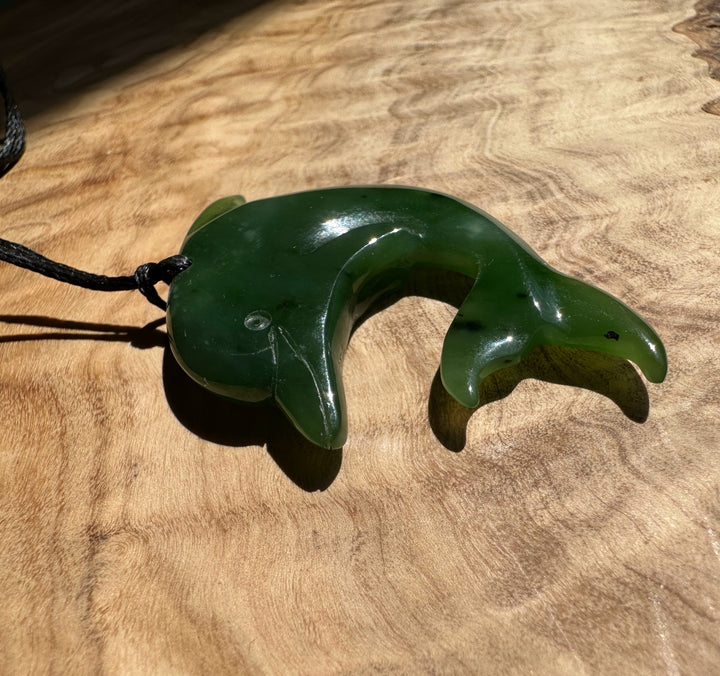 Green jade dolphin pendant with a curved tail on a wooden surface