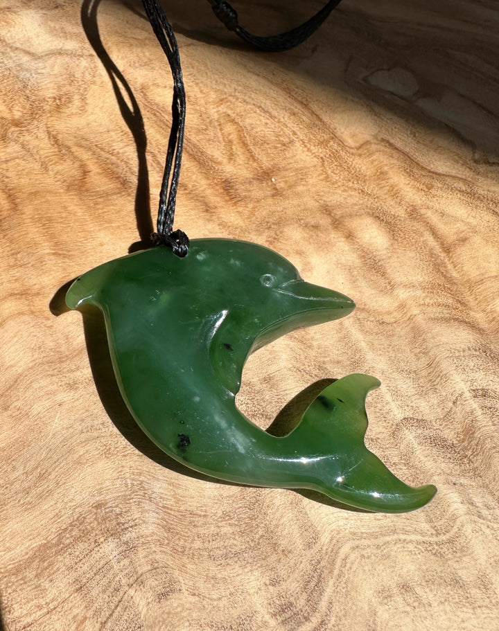 Close up of green jade dolphin pendant on a black cord against a wood background