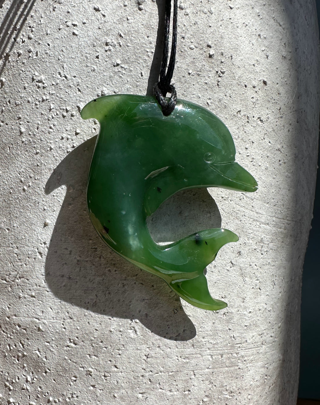 Dolphin-shaped green jade pendant hanging on a black cord