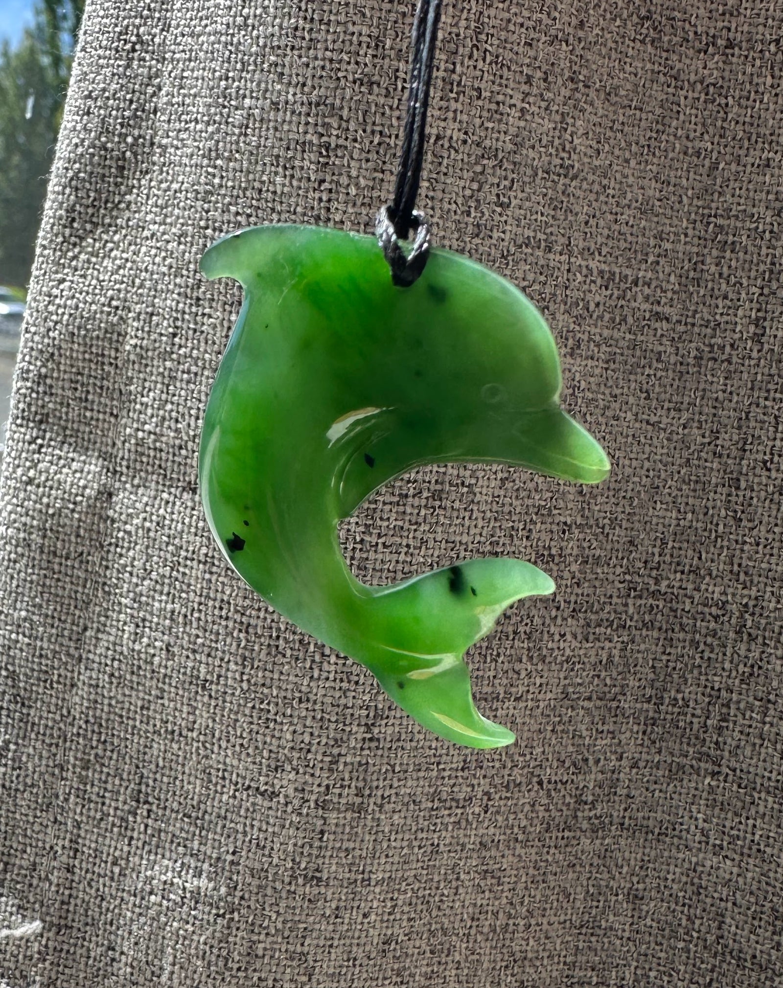 Green dolphin pendant on black cord against brown textured fabric