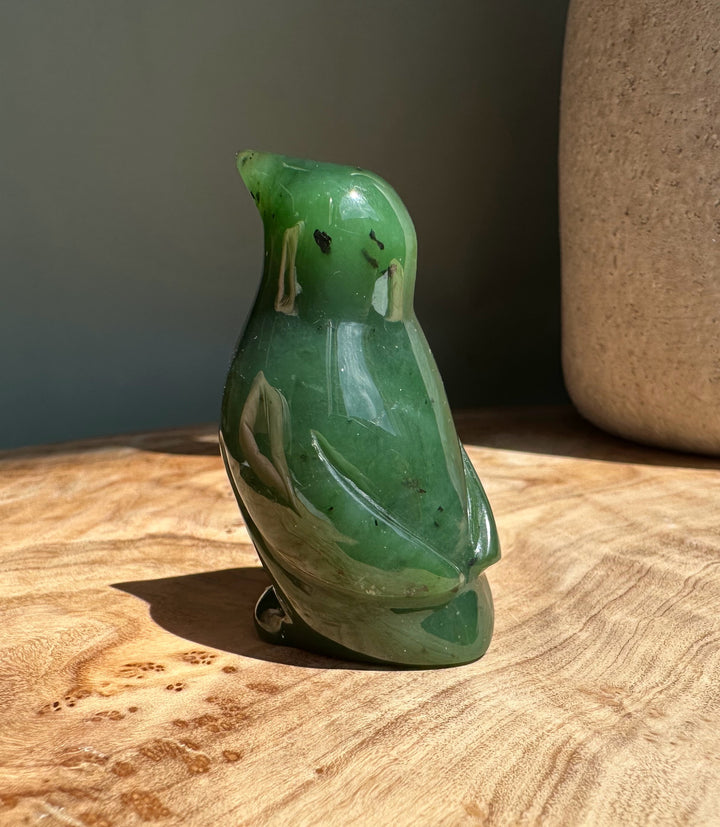 Green nephrite jade penguin figurine with glossy finish on a wooden surface.