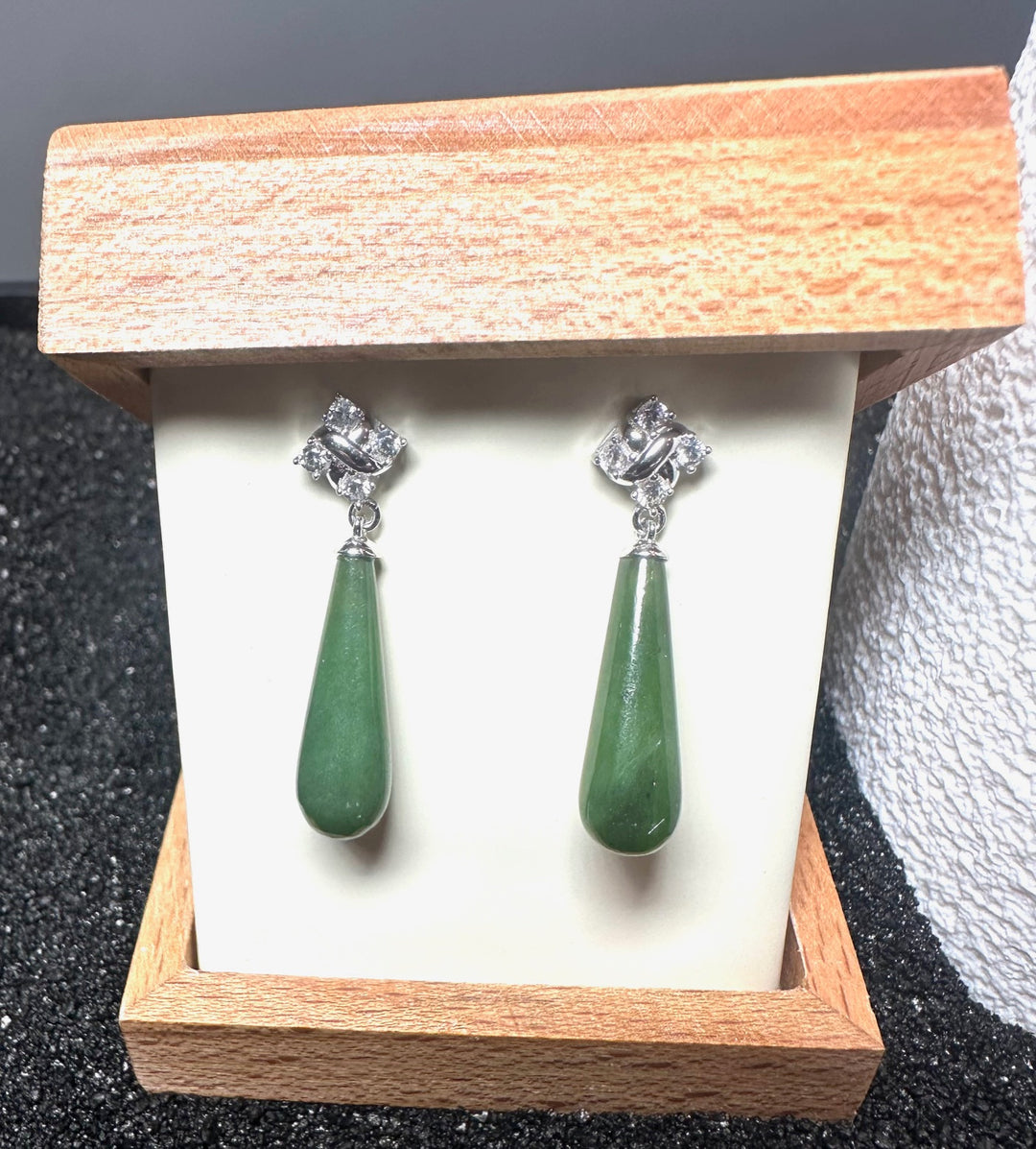 Silver drop earrings featuring green teardrop stones and crystal accents in a wooden jewelry box