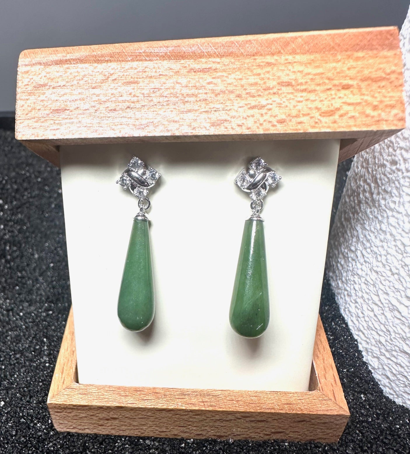 Silver drop earrings featuring green teardrop stones and crystal accents in a wooden jewelry box