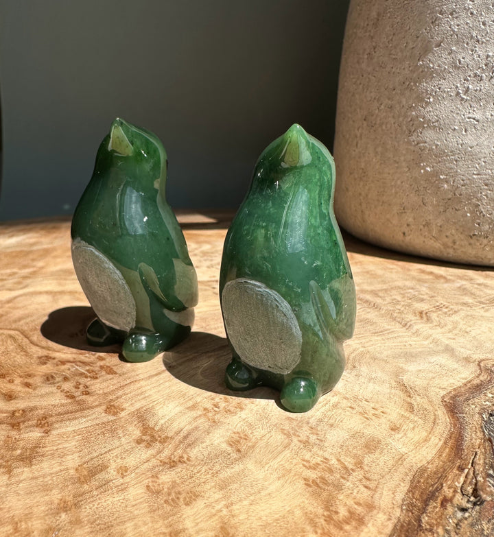 Two nephrite jade penguin figurines viewed from the back on a wooden surface.