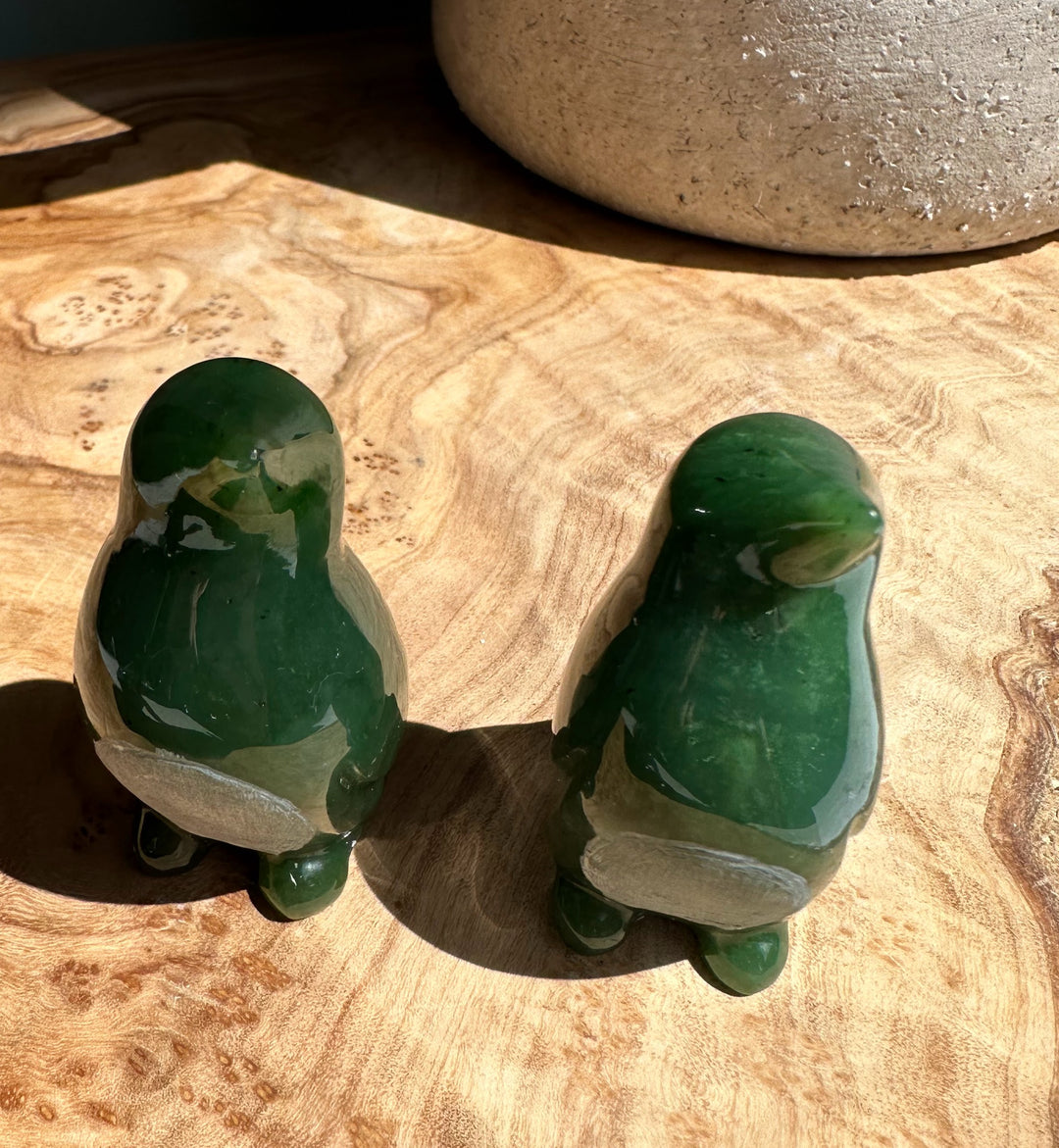 Pair of nephrite jade penguin figurines in dark and light green on a wooden surface