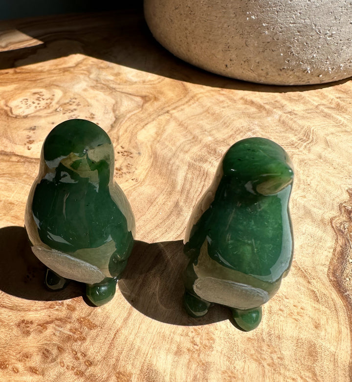 Pair of nephrite jade penguin figurines in dark and light green on a wooden surface
