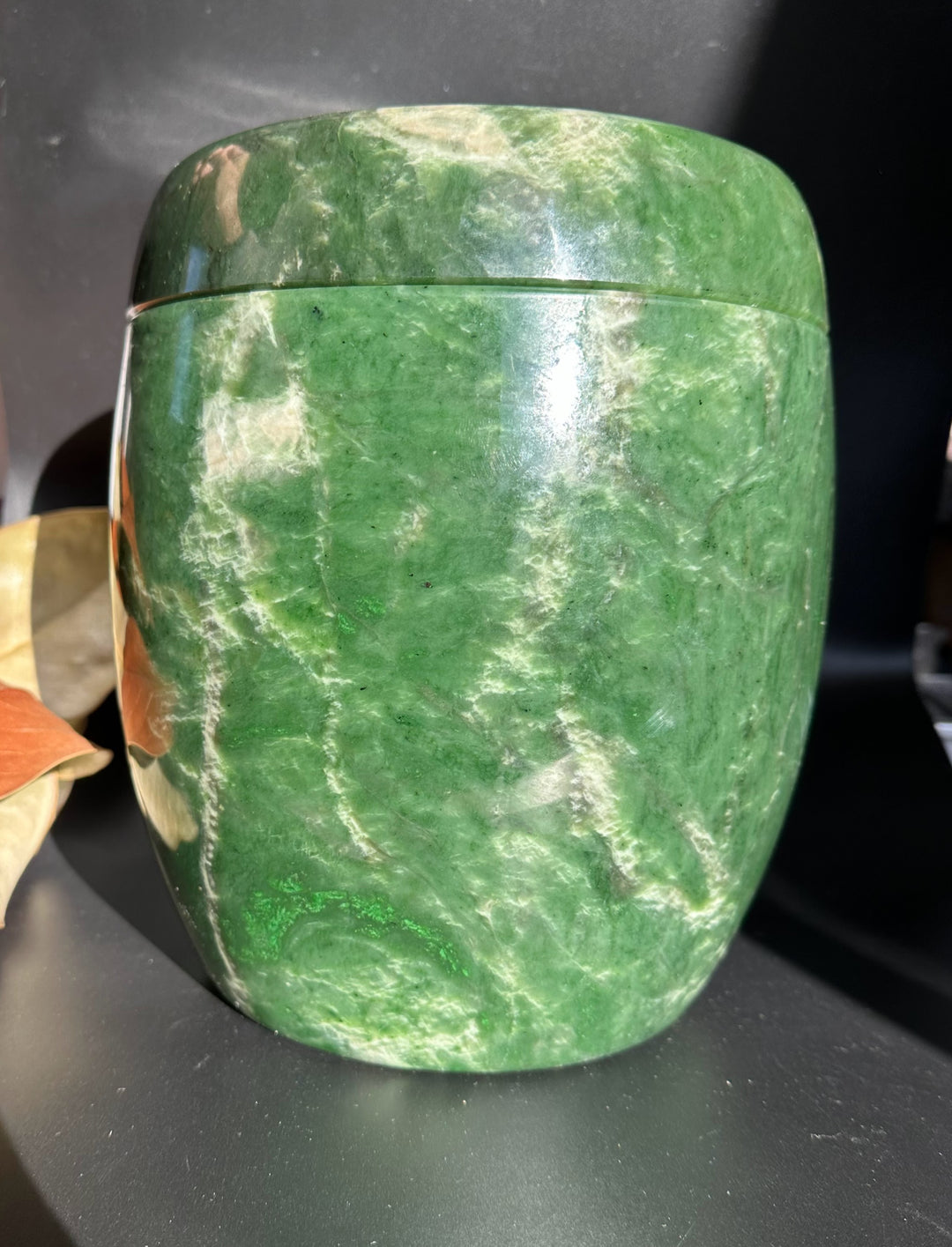 Green jade burial urn with lid on, showcasing smooth polished stone and natural veining