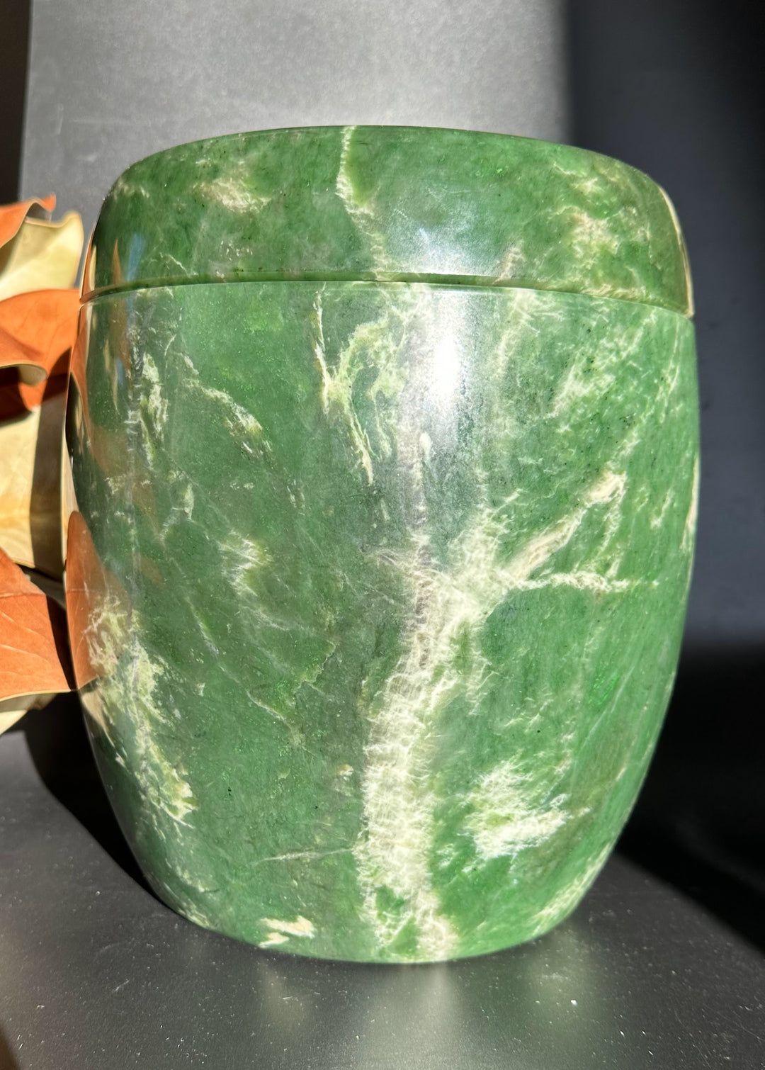 Side view of green jade burial urn with lid in place and white vein patterns.