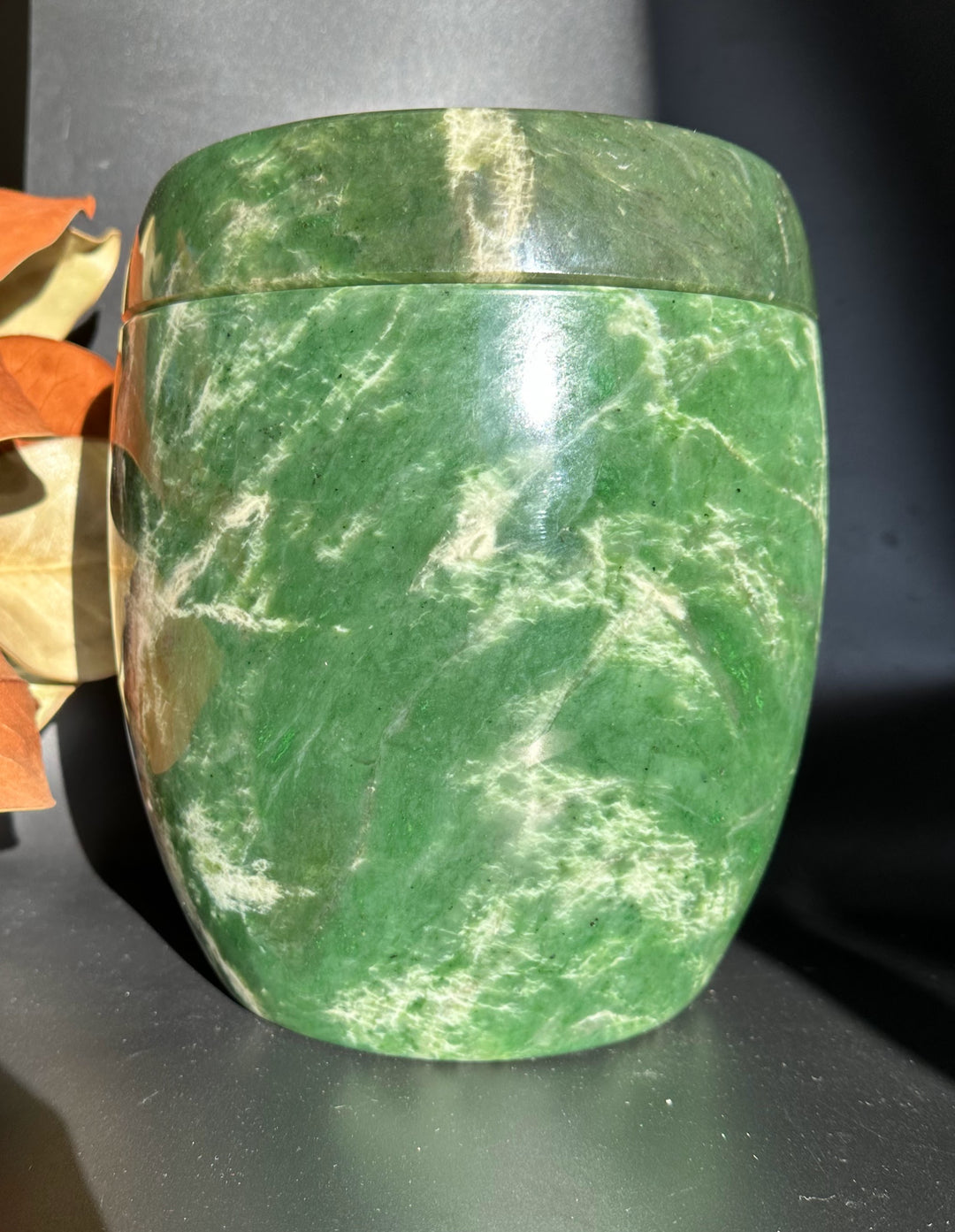 Green jade burial urn with lid in place showing polished surface and white veining.