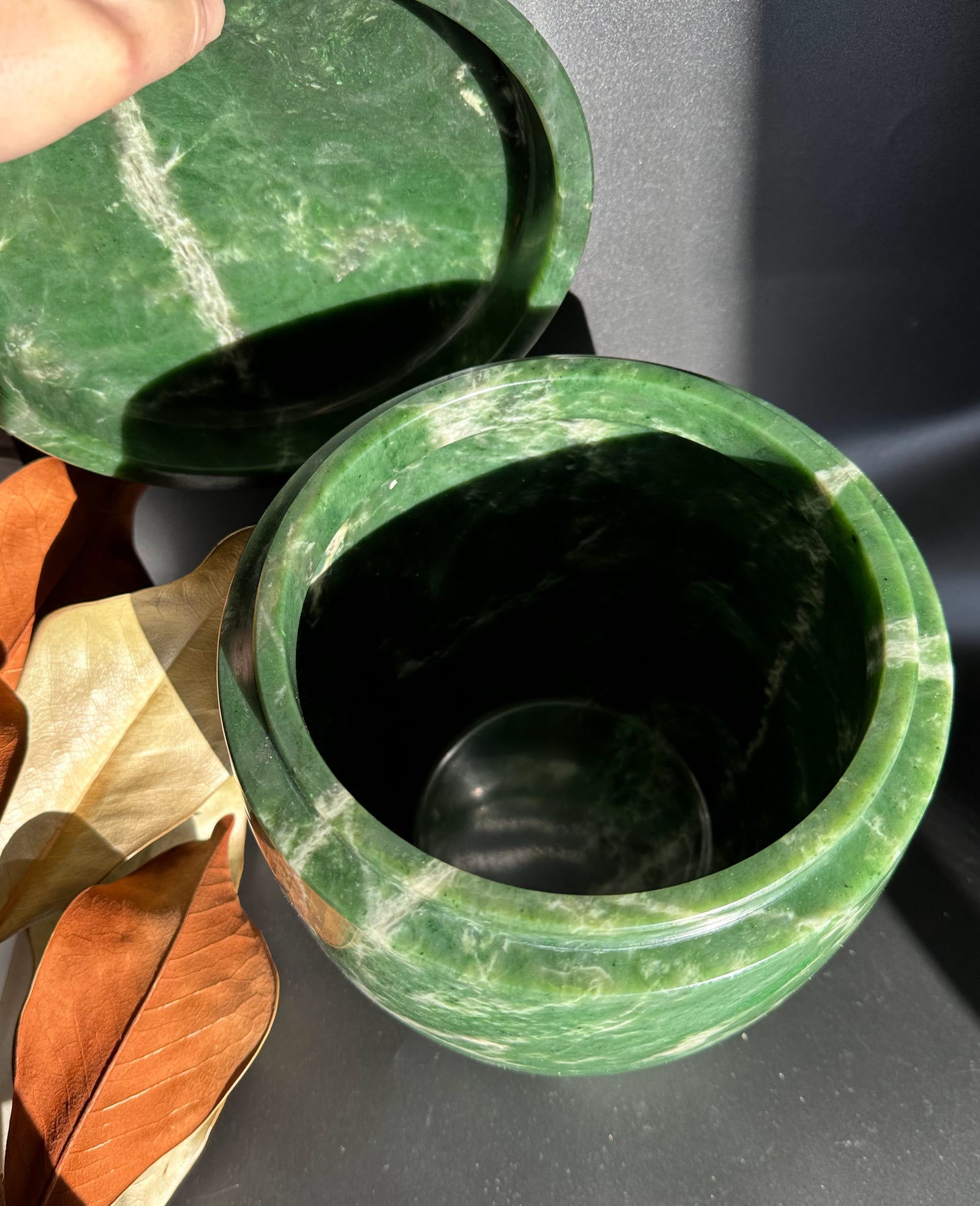 Open green jade burial urn with lid lifted to the side showing a dark interior.