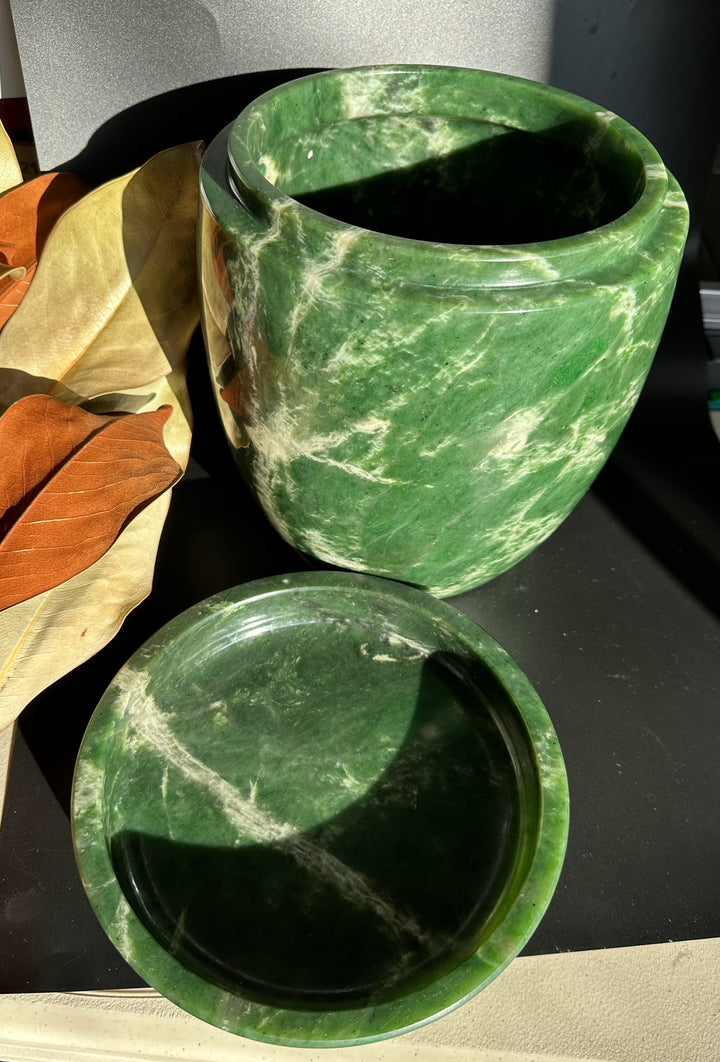 Green jade burial urn with white veining and lid removed, placed beside on a dark surface