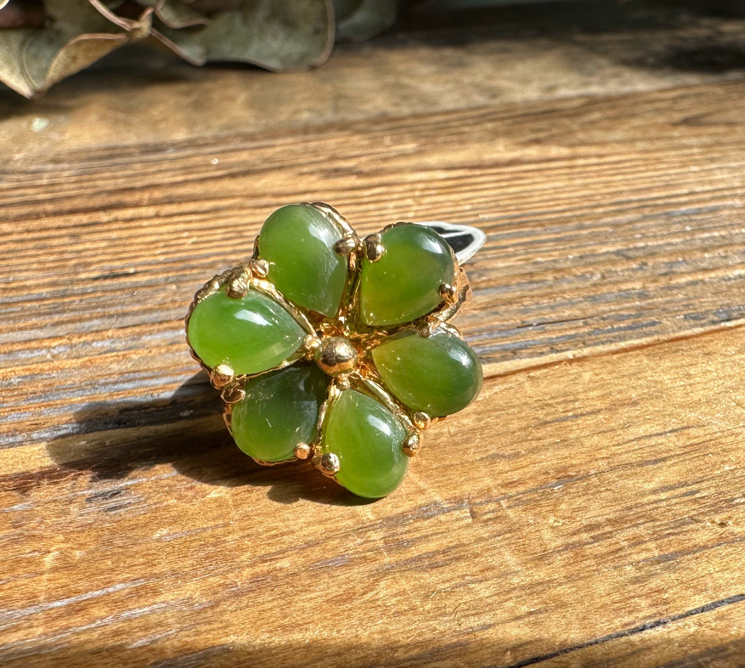 Close up of vintage jade clover ring showing five green heart shaped stones set in gold on a wooden surface.