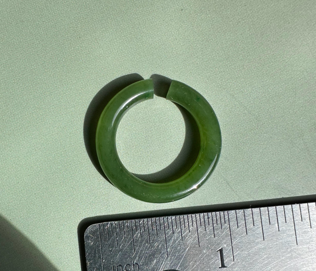 Green jade ear cuff 25mm with a small gap on a green surface beside a ruler for scale