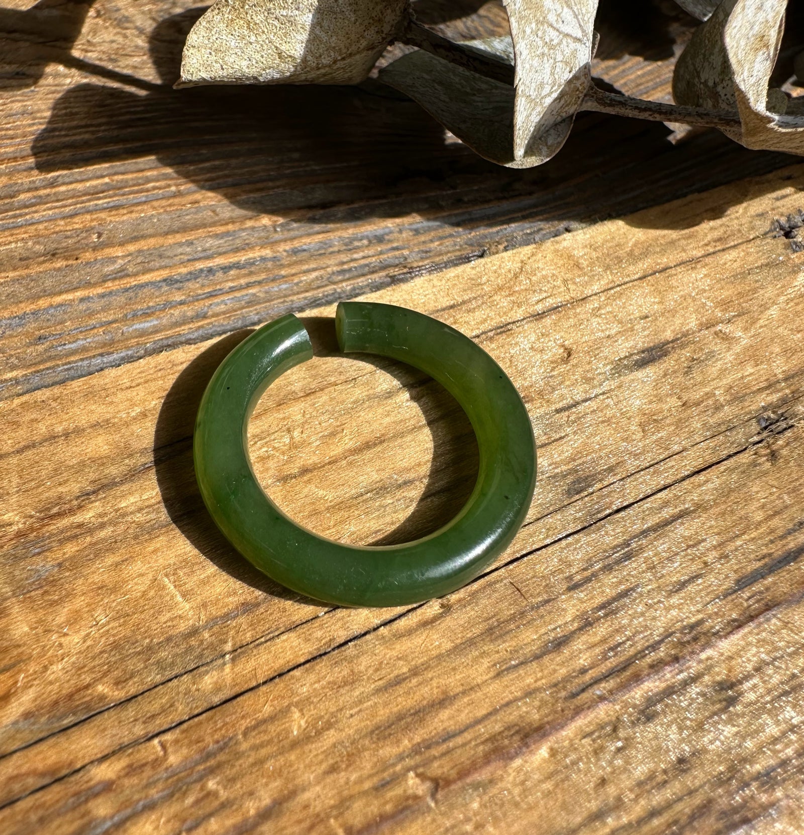 Green circular jade ear cuff with a small opening resting on a wooden surface