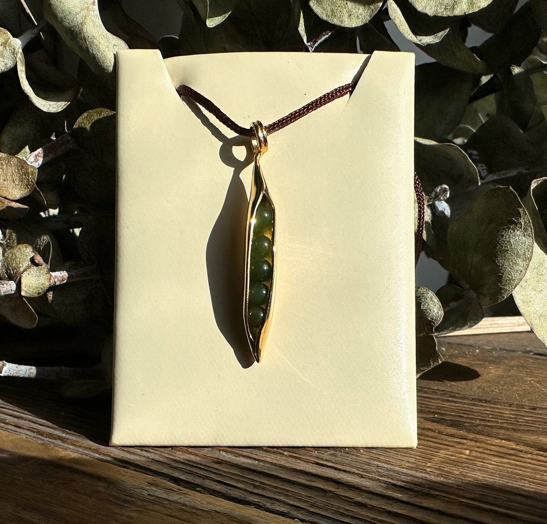 Jade Peapod Pendant in gold tone with green jade beads inside displayed on a beige card