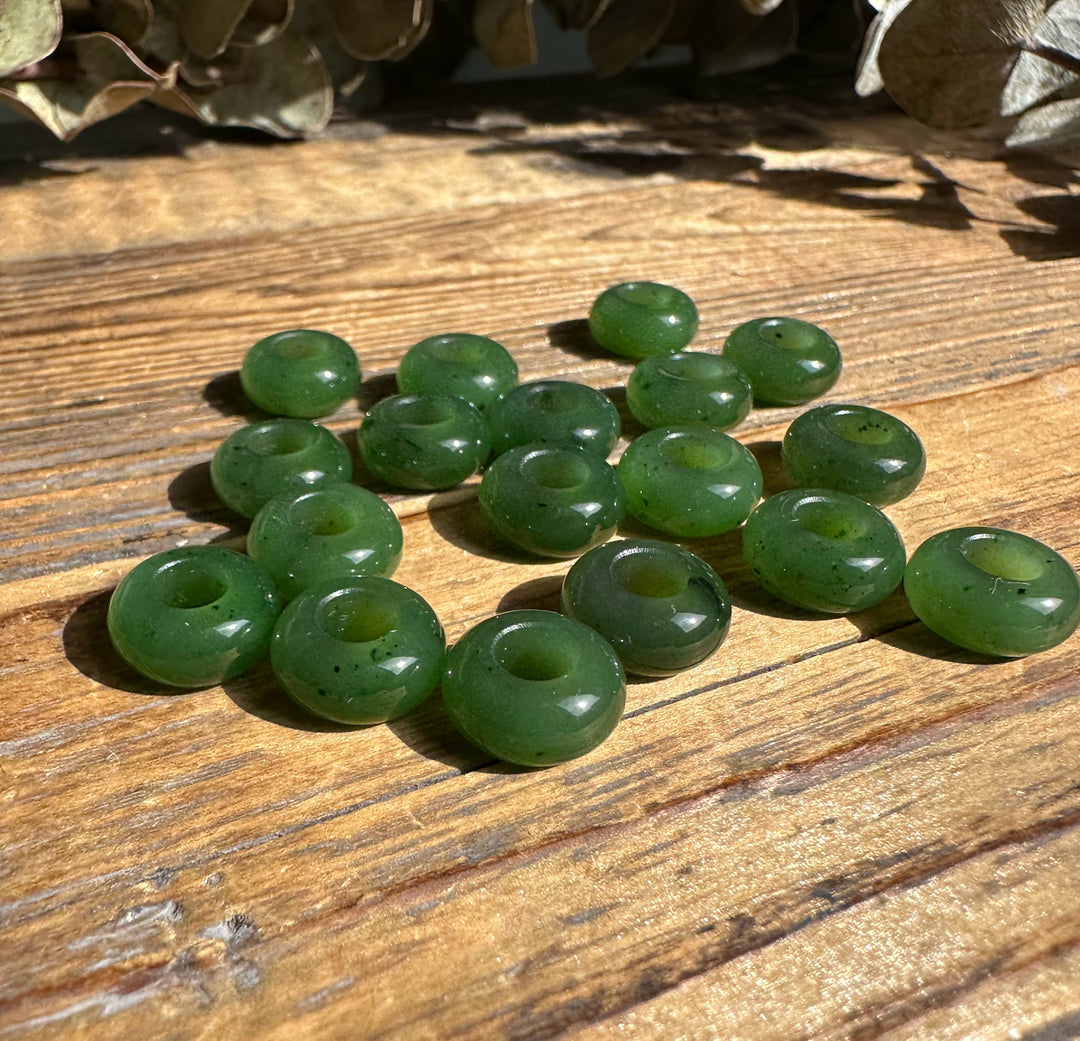 Several green donut beads with central holes scattered on a wooden surface