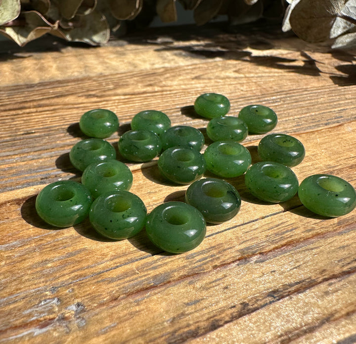 Several green donut beads with central holes scattered on a wooden surface
