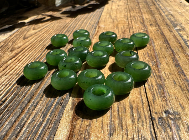 Group of green jade donut shaped beads with holes spread on a wooden surface
