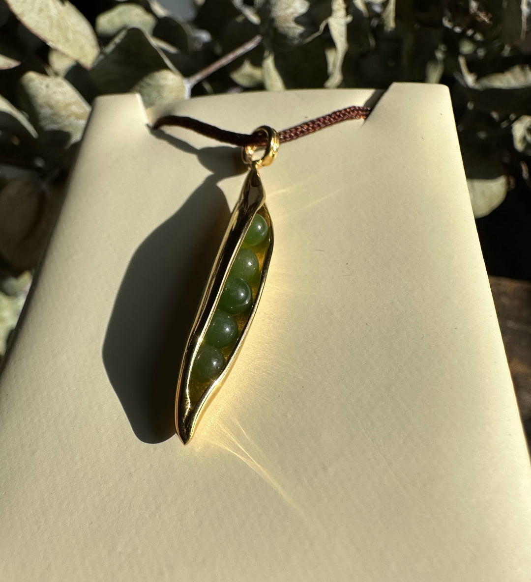 Jade Peapod Pendant in stainless steel with green jade beads nestled in a slim pod