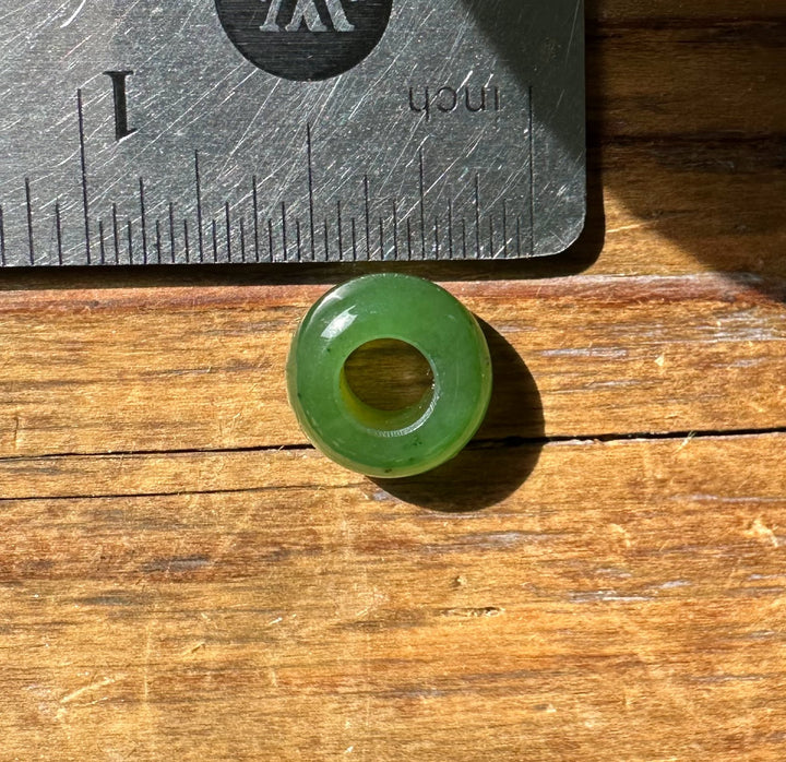 Green 6mm by 12mm donut bead with a central hole beside a metal ruler for scale