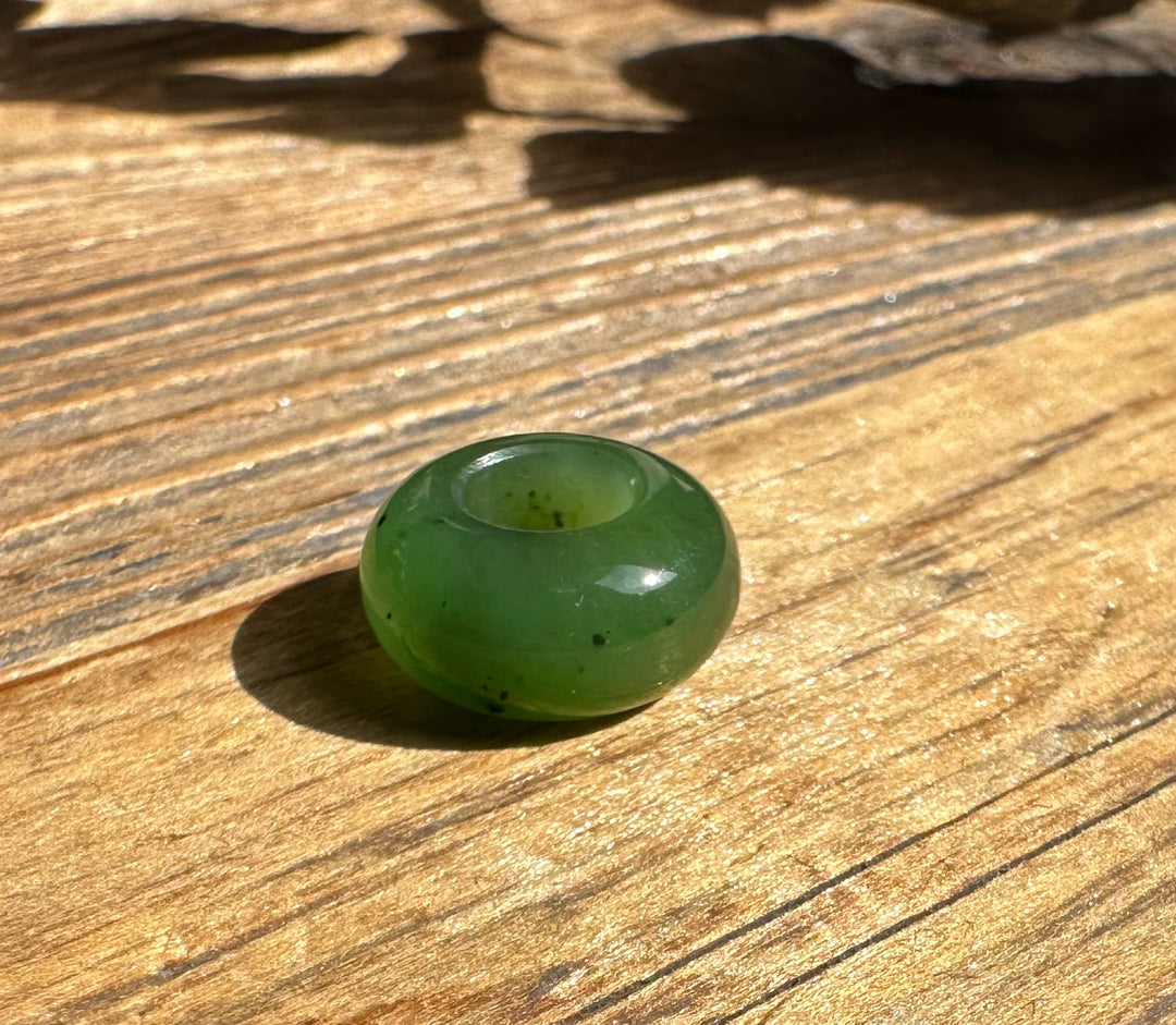 Green 6mm by 12mm donut bead with a central hole on a wooden surface