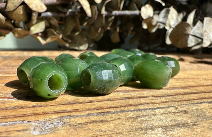 Hand holds several faceted Canadian jade beads with drilled holes.