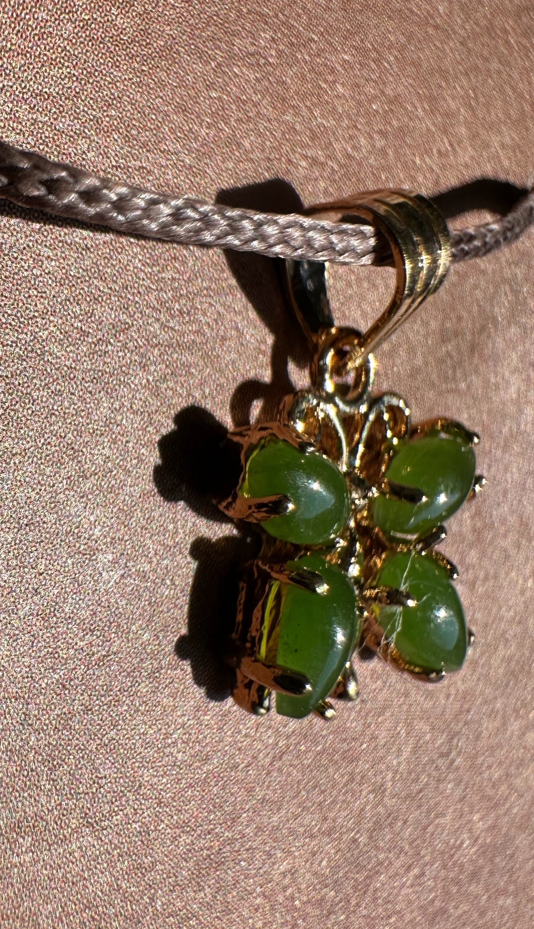 Vintage jade butterfly pendant with green cabochon stones in a gold setting, suspended from a gray braided cord.