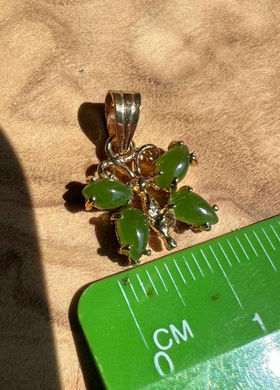 A grade vintage jade butterfly pendant with six green teardrop stones in a gold setting beside a centimeter scale.