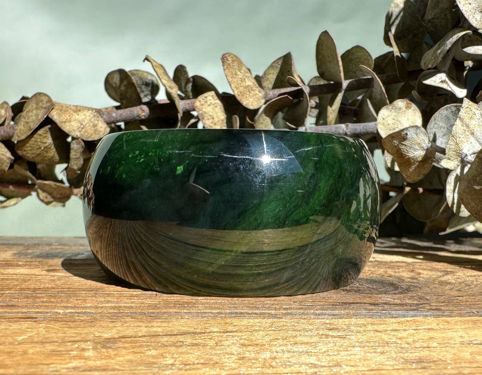 Dark green wide jade bangle with a smooth polished finish resting on a wooden surface