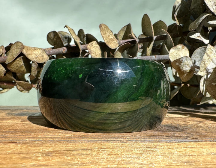 Dark green wide jade bangle with a smooth polished finish resting on a wooden surface
