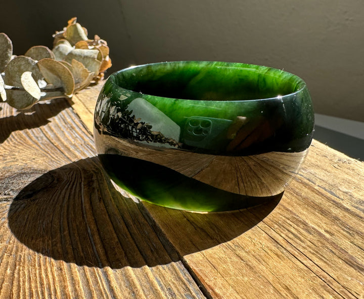 Side view of a dark green jade bangle with layered banding on a wooden table.