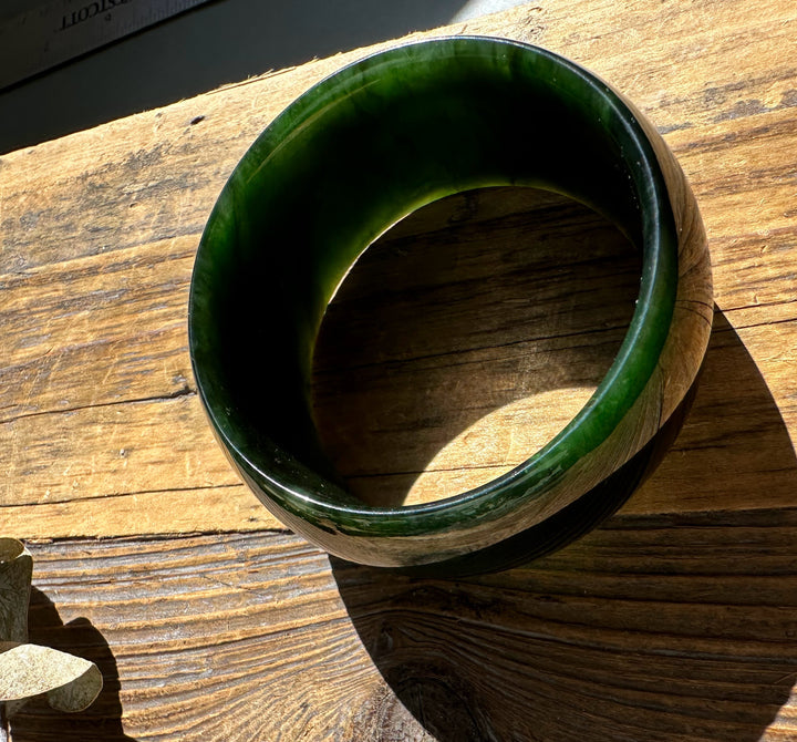 Dark green polished jade bangle with a wide profile resting on a weathered wooden surface.