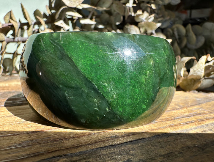 Dark green A Grade wide jade bangle with a polished glossy finish resting on a wooden surface.