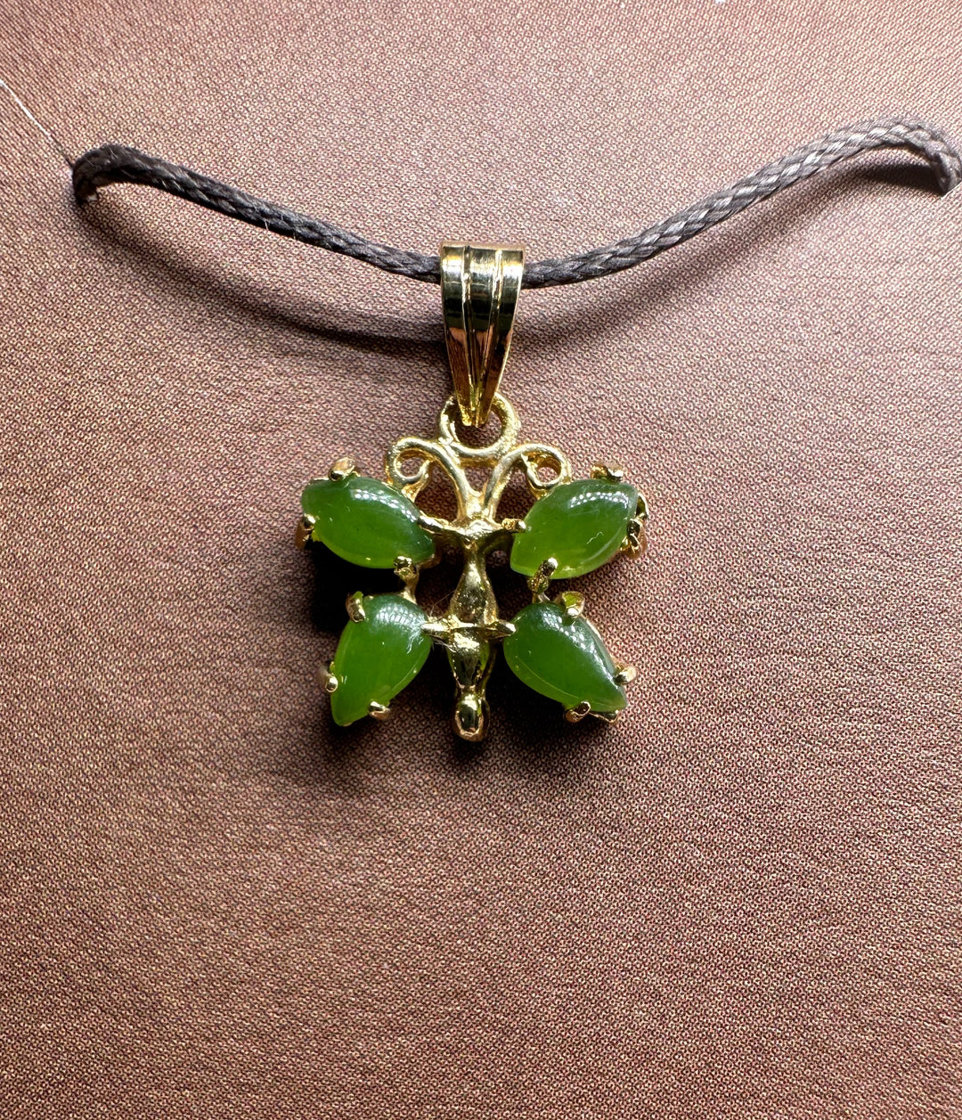 Vintage jade butterfly pendant with green stones in a gold setting on a dark braided cord necklace.