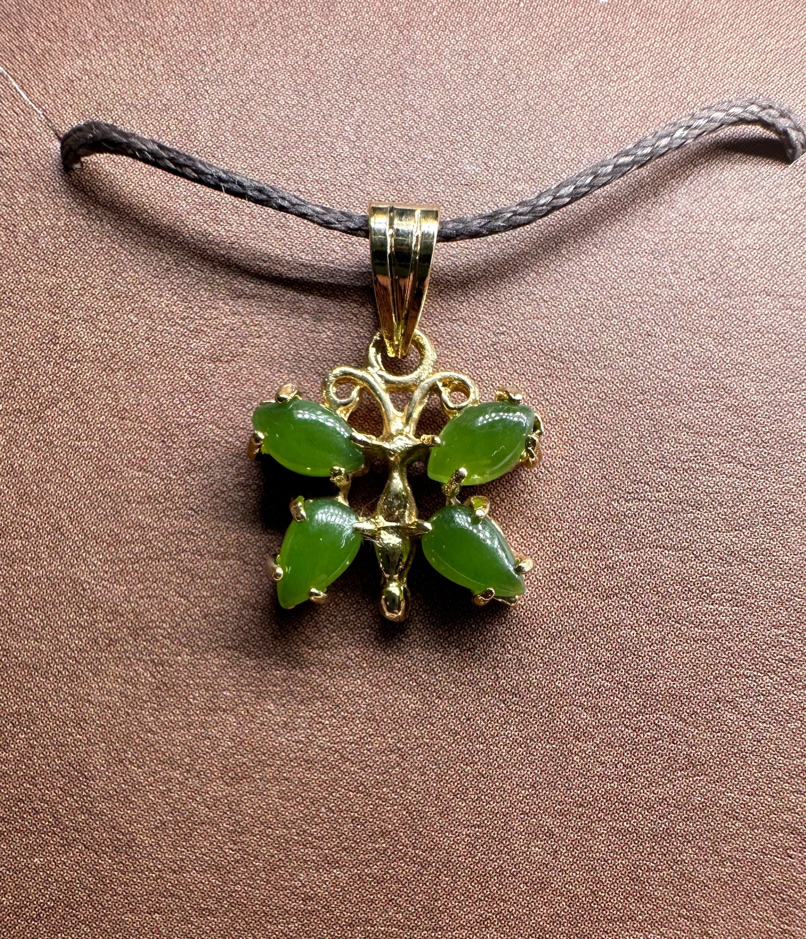 Vintage jade butterfly pendant with green stones in a gold setting on a dark braided cord necklace.