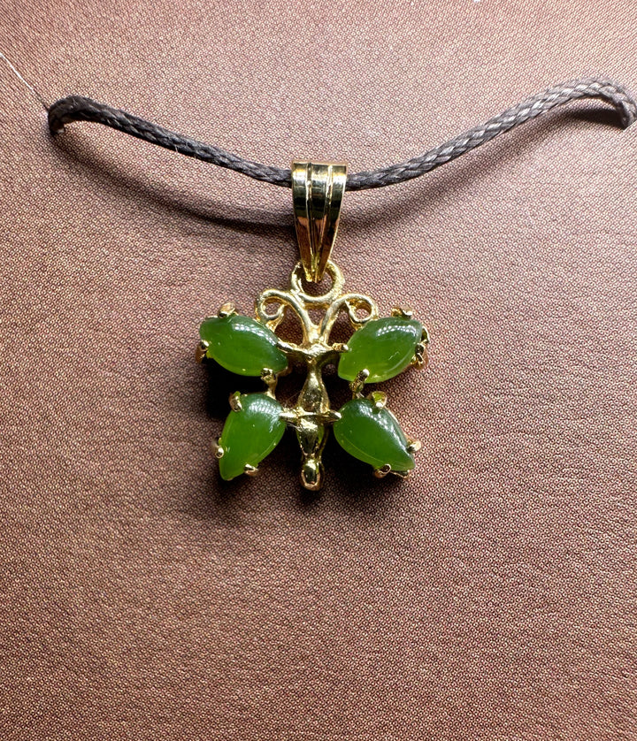 Vintage jade butterfly pendant with green stones in a gold setting on a dark braided cord necklace.