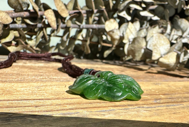 Green jade butterfly pendant resting on a wooden surface with dried leaves in the background