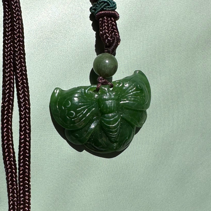 A Grade Ogden Jade Butterfly Pendant in dark green hanging from a burgundy braided cord with a green bead