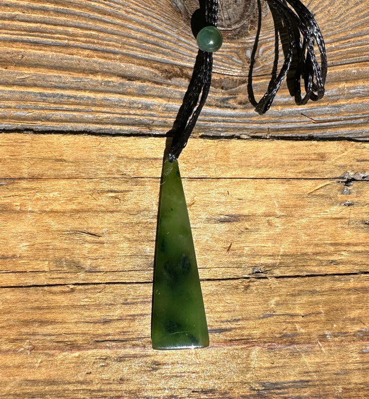 Green jade drop pendant with round bead on black cord shown against rustic wood background