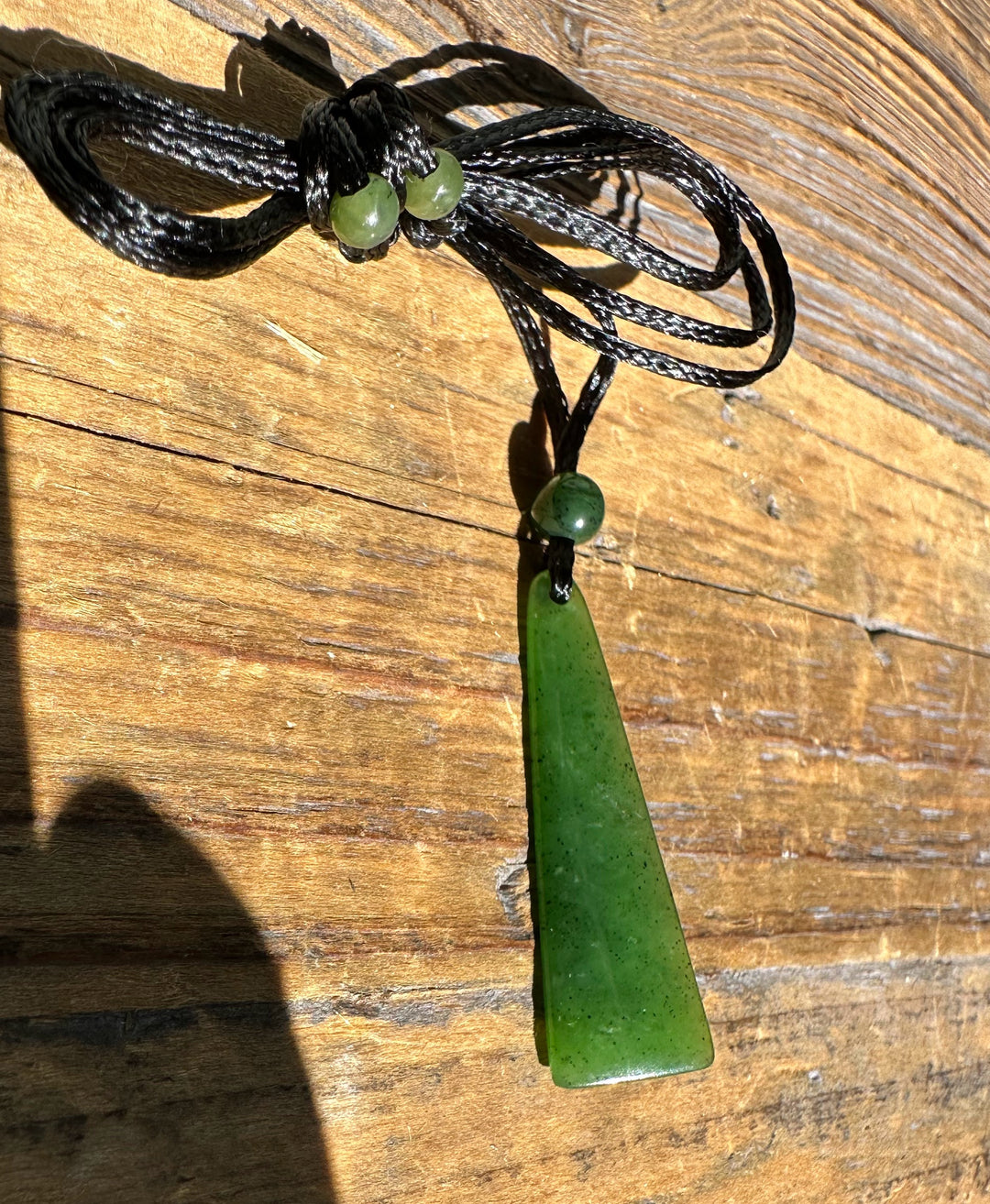 Canadian jade drop pendant with beads on a black cord shown against a wooden surface